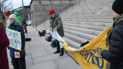 Klimatdemonstranter på riksdagens trappa sätter upp en banderoll.