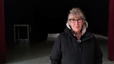 Medelålders kvinna poserar fram en scen i ett föreningshus. 