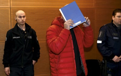 En man i dunjacka döljer ansiktet. I bakgrunden en väktare och en polis.