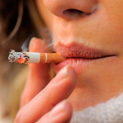 Närbild av en kvinna som röker. I bild syns endast hennes läppar, tobaken och hennes fingrar runt tobaken.