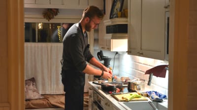 Jan- Christian Forsman står i köket och lagar mat, han skalar lök. 
