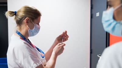 En sjukskötare håller i en dos med coronavaccin samt en spruta. Hon har munskydd på sig.