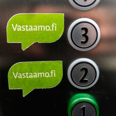 Knappar i en hiss. Gröna lappar tillhörande psykoterapicentret Vastaamo till vänster om siffrorna 2 och 3.