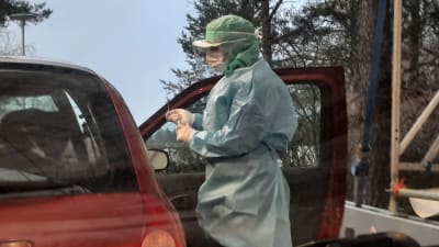 Sjukvårdare i skyddsutrustning tar coronatest på en person i en bil.