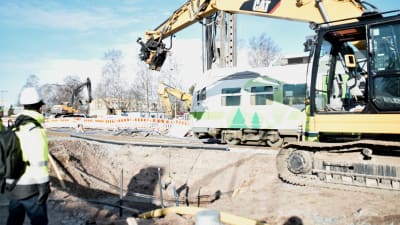 Rälsbussen passerar en grävmaskin vid en grop.