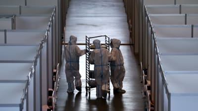 Tre sjukvårdare i full skyddsutrustning går längs en korridor i ett tillfälligt coronasjukhus.