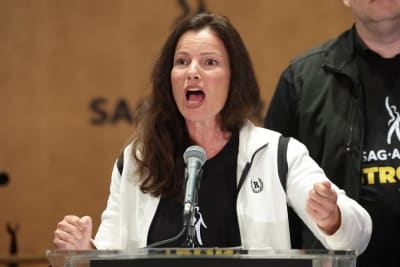 En mörkhårig kvinna står framför en mikrofon och talar passionerat.
