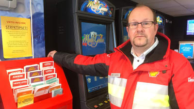 Spelombudet Anders Holmberg lutar mot en ställning med Lottokuponger.
