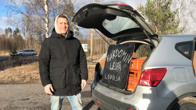 En man vid sin bils baklucka. I bakluckan finns det en skylt där det står Hardomin leipä Loviisa.