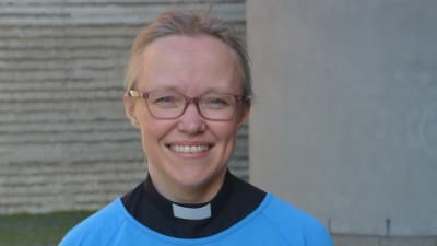 Kvinna med prästkrage och ljusblå tunika som ler