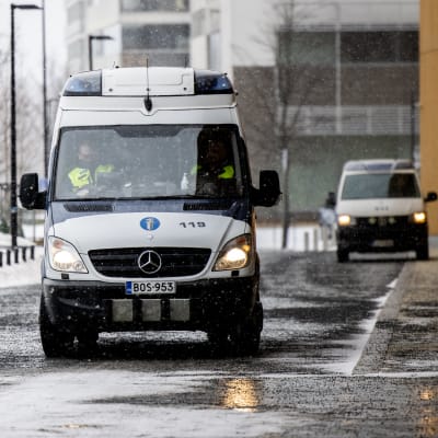 Två av polisens skåpbilar utanför en byggnad i Helsingfors i slaskigt väder.