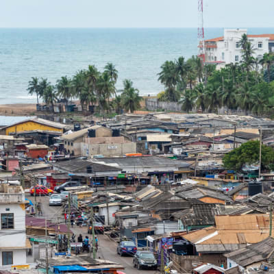 En stadsvy med låg bebyggelse, palmer och hav i Accra, Ghana.