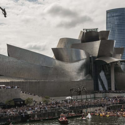 En person gör ett konsthopp från ett tak framför Guggenheim Bilbao.