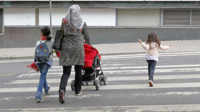 En kvinna med sjal på huvudet går med sina barn över en gata.