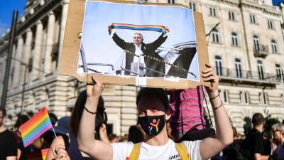En demonstrant håller upp ett plakat med en bild på premiärminister Viktor Orbán. På bilden har någon redigerat in en regnbågsflagga som Orbán håller i.