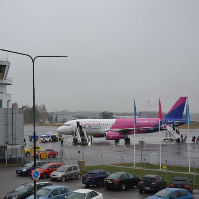 Wizz airs flyg i vitt, rosa och blått har landat på Åbo flygplats och folk håller på att stiga ur planet.