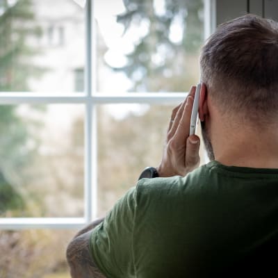 En man pratar i telefon samtidigt som han tittar ut genom ett fönster.