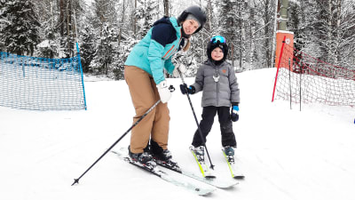 En kvinna och ett barn på slalomskidor i slalombacke. De ser in i kameran och ler.