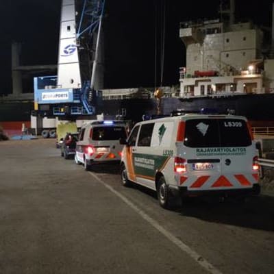 Bild av myndigheternas bilar som står parkerade invid ett fraktfartyg i mörkret. 