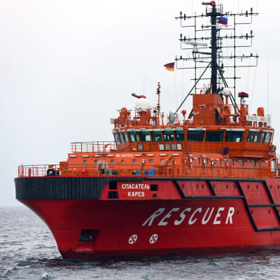 Ett rött-orange färgat fartyg åker på vattnet. På fartyget står det "Spasatel Karev" och "Rescuer".
