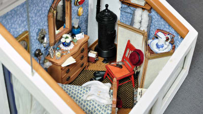 sovrummet består av säng, byrå, stol, speglar, klockor och smycken, en kamin, hattar och tavlor. 