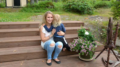 Kvinna med barn i famnen sitter på trappa utomhus