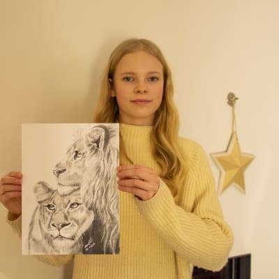 En ung tjej håller upp en teckning av två lejon, som hon själv har gjort.
