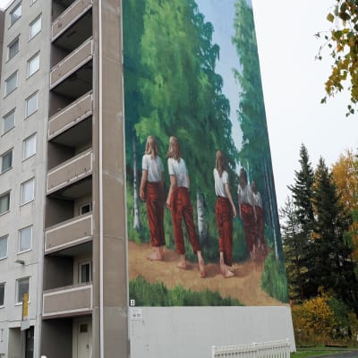 Kerrostalo, jonka seinässä on iso seinämaalaus, jossa tyttö kävelee metsässä.