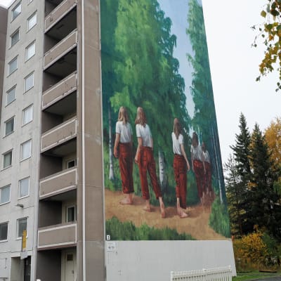 Kerrostalo, jonka seinässä on iso seinämaalaus, jossa tyttö kävelee metsässä.