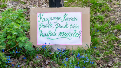 En skylt lutad mot en stolpe. På skylten har någon på finska skrivit en kort dikt om att stadens vackraste park snart är bara ett minne.