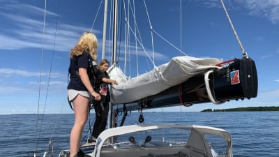 Två tonårsflickor står uppe på taket på en segelbåt ute till havs, redo att hissa segel. 