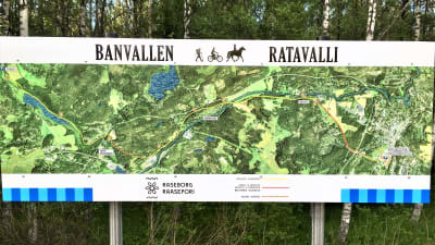 En karta som med en bild tagen från luften visar hur den nya friluftsleden i Raseborg, Banvallen, löper från Karis via Billnäs och Åminnefors till Skuru och Fiskars bruk.