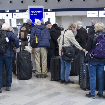 Matkustajia lentokentällä matkalaukkujen kanssa. 
