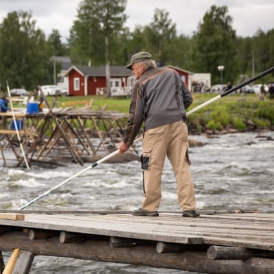 Mies lippoaa Kukkolankoskella, taustalla mies lippoaa Kukkolaforssenilla Ruotsin puolella.