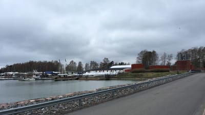 Bron till Björkholmen från Drumsö. Himlen är mulen, havet grått. På bilden syns båtar uppe på land och röda magasinbyggnader.