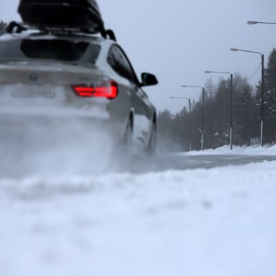 Auto ajaa talvisella tiellä, lumi pöllyää.