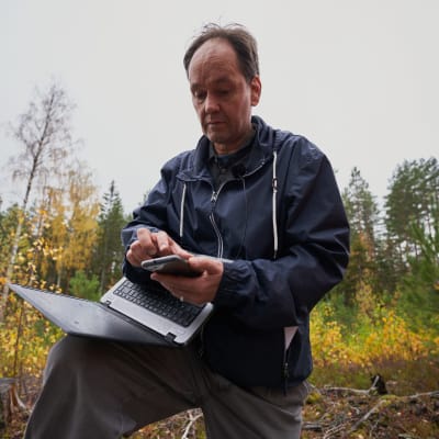 Jari Natunen skriver på sin mobiltelefon i skogen. 