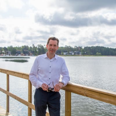 En man i kragskjorta står på en träbro och tittar in i kameran.