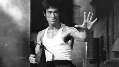 Bruce Lee ojentaa vasenta kättään eteen, oikeassa kädessä nunchaku.
