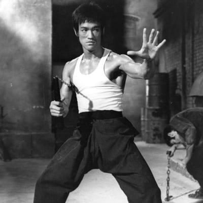 Bruce Lee ojentaa vasenta kättään eteen, oikeassa kädessä nunchaku.