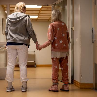 En vårdare leder en äldre boende i en korridor.