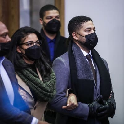 Jussie Smollett i munskydd utanför en domstol i Chicago. Han är klädd i en grå kappa, svart halsduk och svarta läderhandskar. 
