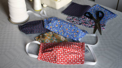 Munskydd av tyg i olika färger och mönster ligger på ett bord bredvid en symaskin.