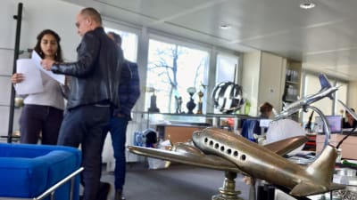 Bertrand Piccard talar med ett par anställda på hans stiftelse och i förgrunden ser vi en statyett av ett flygplan från mellankrigstiden.