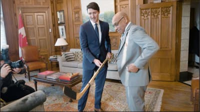 Justin Trudeau och Willy O'Ree beundrar en hockeyklubba.