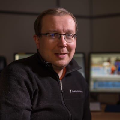 man sitter med dataskärmar bakom sig