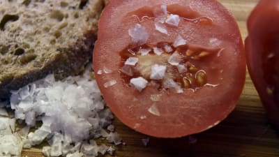 Många tillsätter salt i sin mat för att få mer smak. På bilden syns salt på en tomat och på vänster sida syns en brödbit.