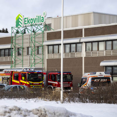 Ekovillan tehdasrakennuksen edessä kaksi paloautoa ja yksi ambulanssi. Etualalla näkyy lumipenkkaa.