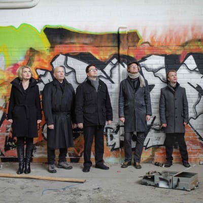 Uusinta Ensemblen muusikot seisovat graffitiseinän edessä yläviistoon katsoen.