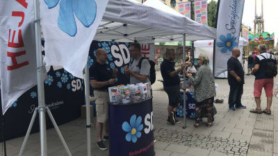 Sverigedemokraterna gör valkampanj och talar med förbipasserande på en gågata.